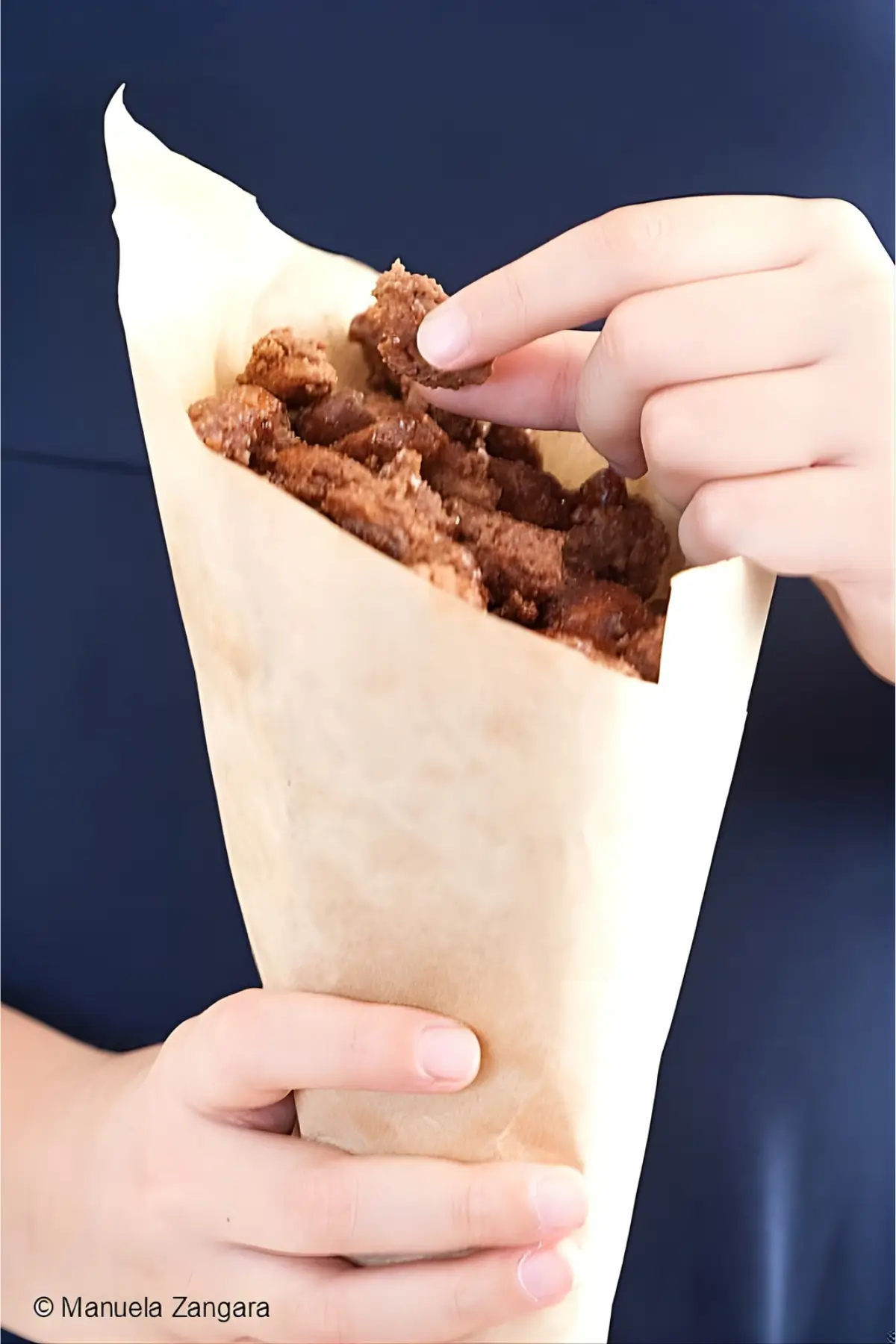 Hand reaching into a paper cone of almond pralines.