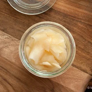 A small glass jar of pickled ginger placed on a wooden board.