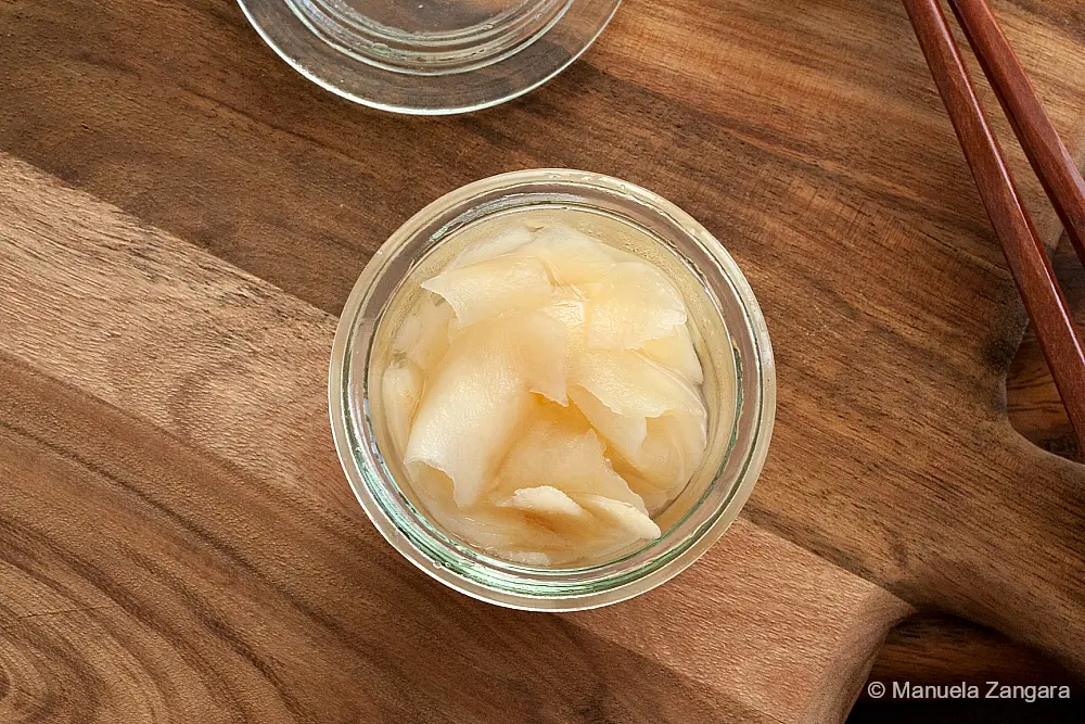 A small glass jar of pickled ginger placed on a wooden board.
