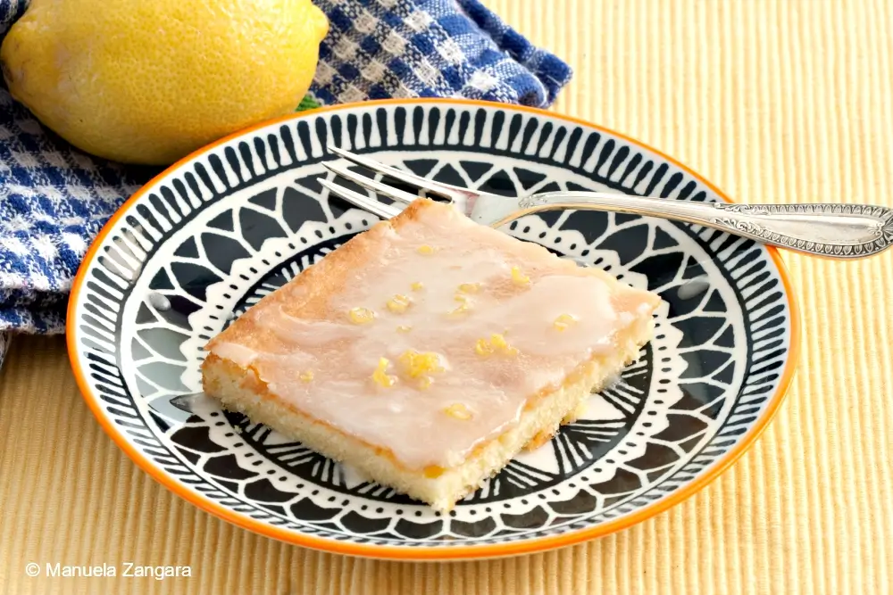 Closeup of a glazed low FODMAP lemon cake square topped with lemon zest.