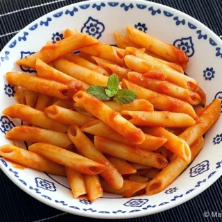 Bowl of penne coated in tomato sauce with a mint leaf on top.