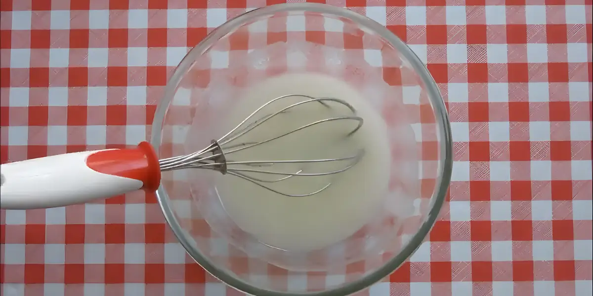 Lemon glaze being mixed in a glass bowl with a whisk.