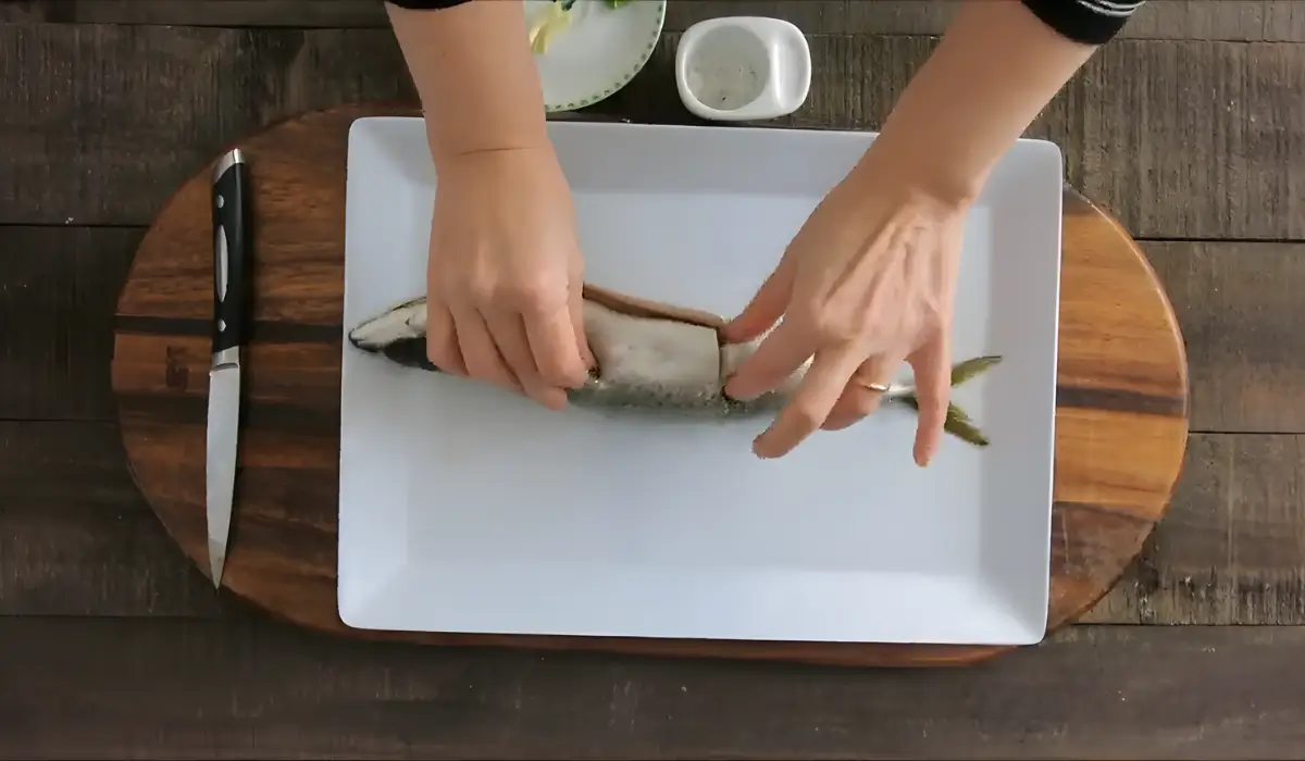 Hands filling slits in a whole mackerel with garlic and mint.