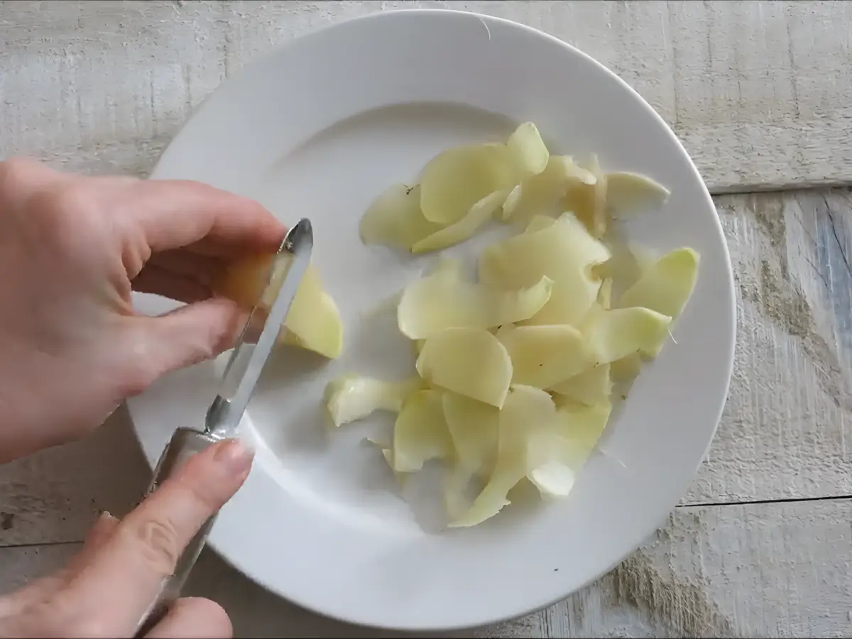 Thin slices of young ginger being prepared on a plate.