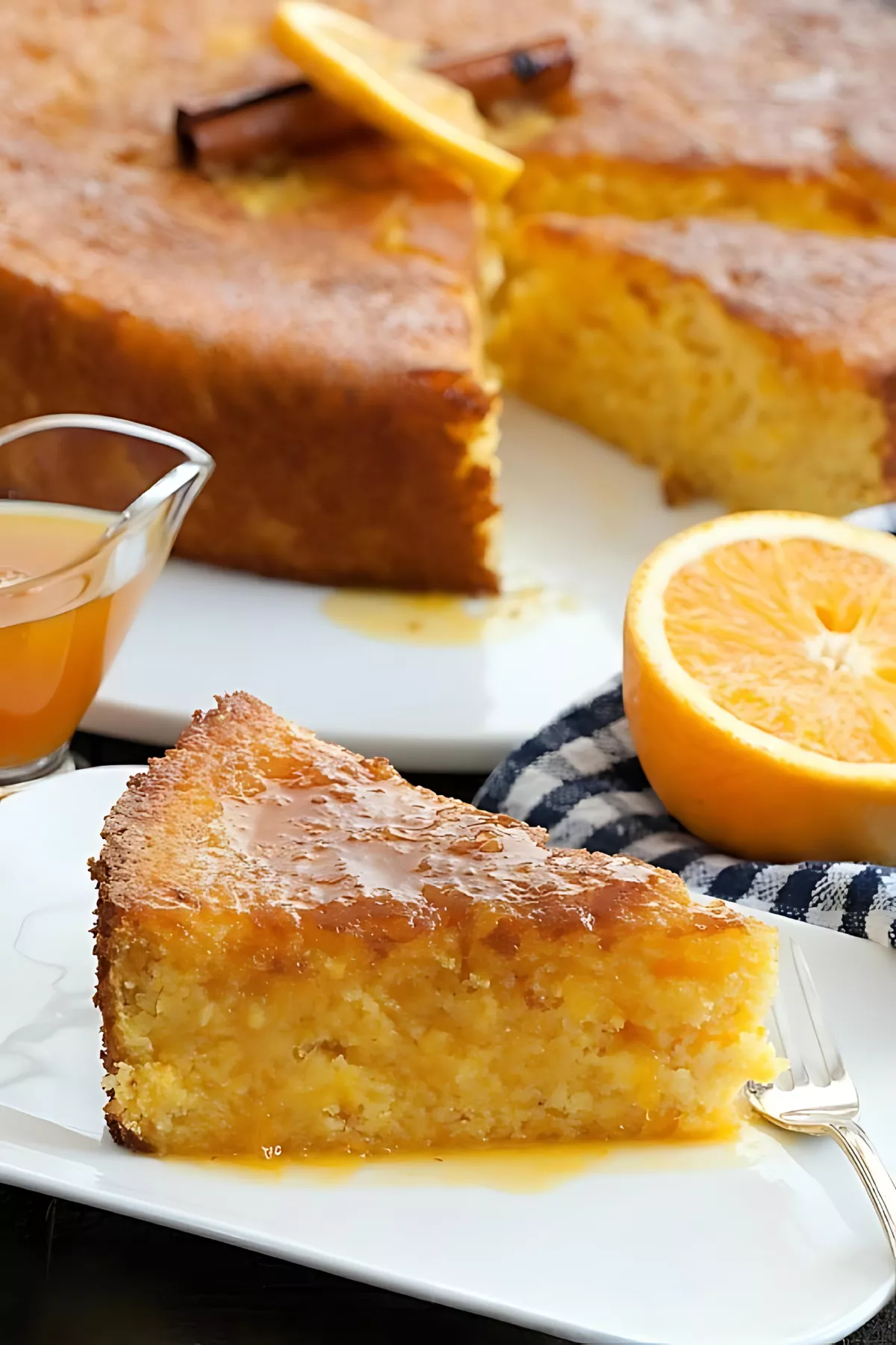 Slice of gluten-free orange polenta cake drizzled with syrup beside fresh orange halves.