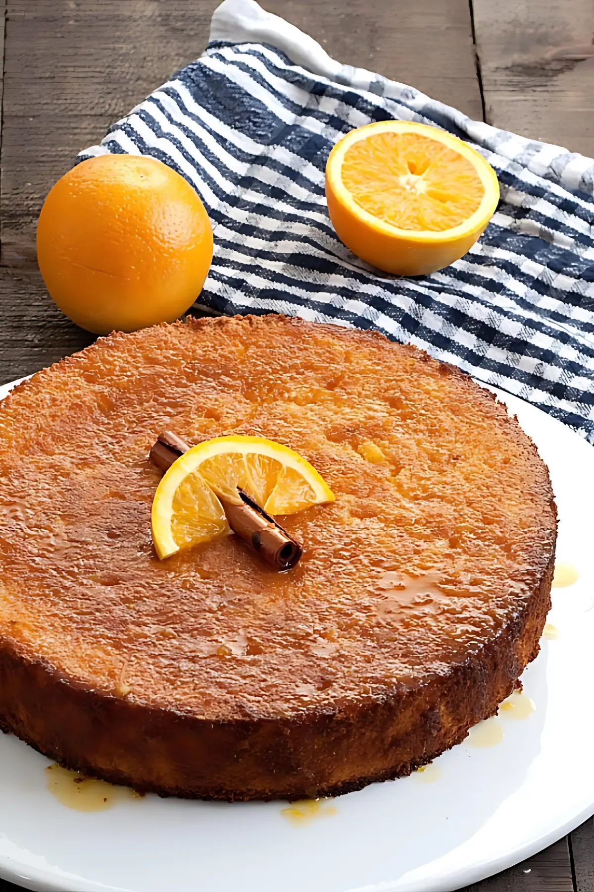 Whole orange polenta cake topped with orange slice and cinnamon stick on a white plate.