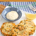 Low FODMAP salmon cakes served with creamy aioli and a lemon wedge on a white plate.