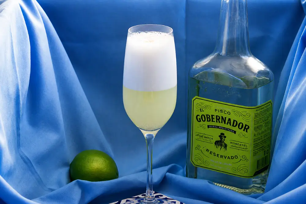 Chilled cocktail with creamy foam served in a tall glass with fresh lime on the side.