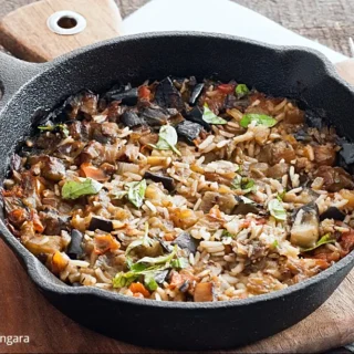 Overhead shot of cooked eggplant rice in a cast iron pan with basil.