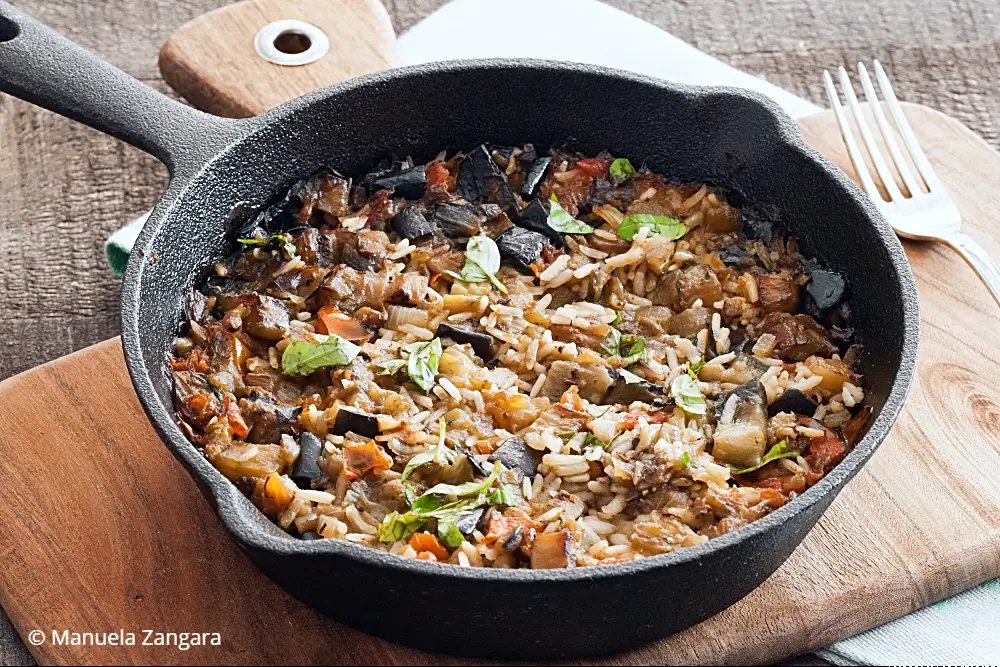 Overhead shot of cooked eggplant rice in a cast iron pan with basil.