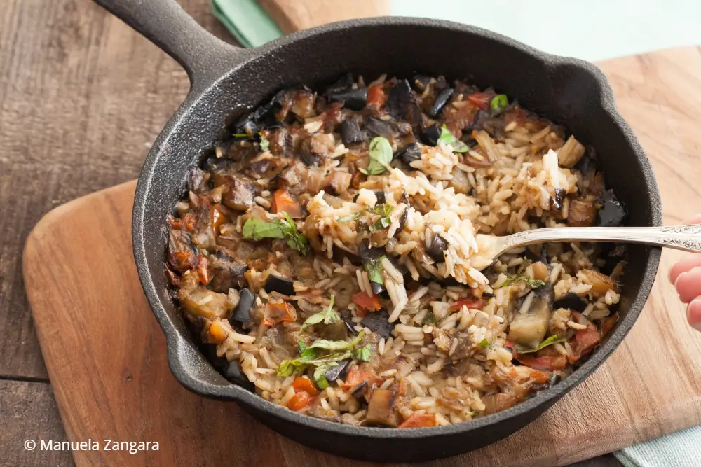 Cooked eggplant rice in a cast iron skillet with a fork lifting a serving.