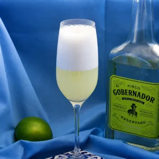 Frothy Pisco Sour served in a tall glass with creamy foam and pale citrus base.