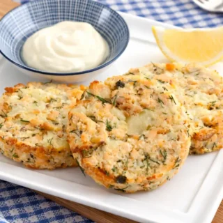 Low FODMAP salmon cakes served with creamy aioli and a lemon wedge on a white plate.