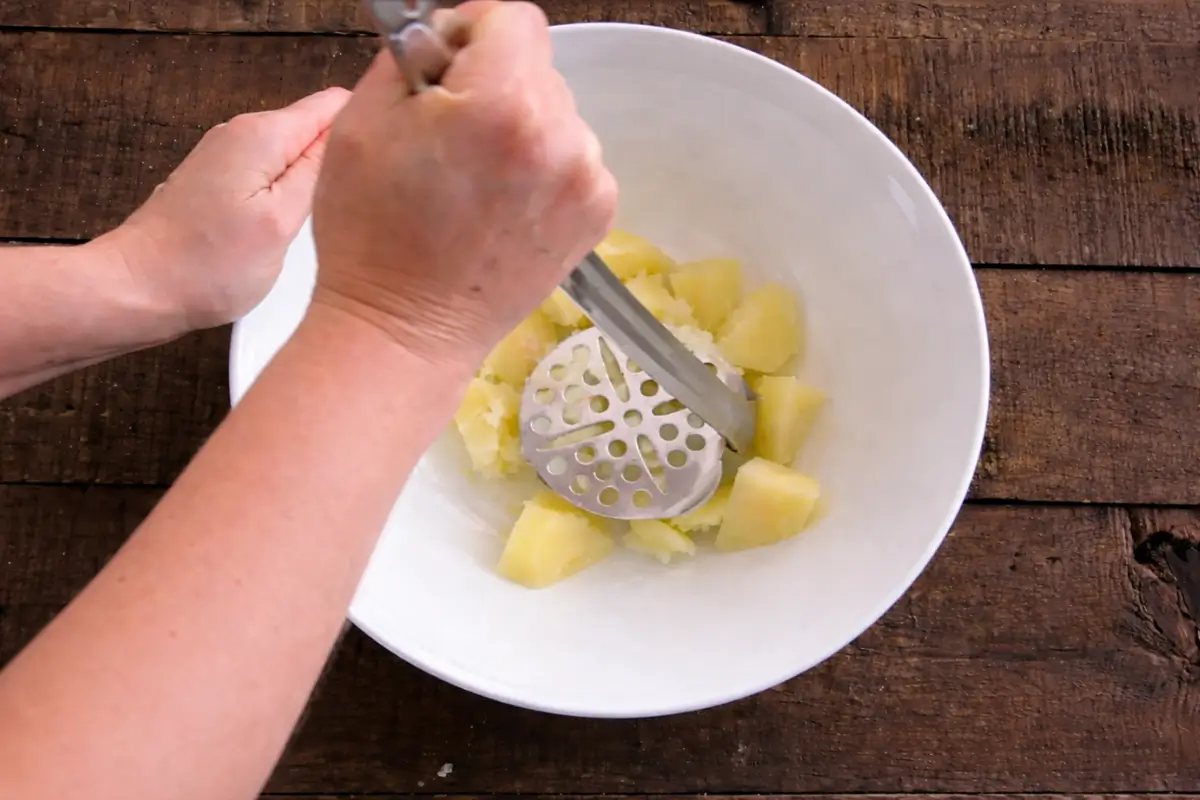 Boiled potatoes being mashed until smooth in a large bowl.