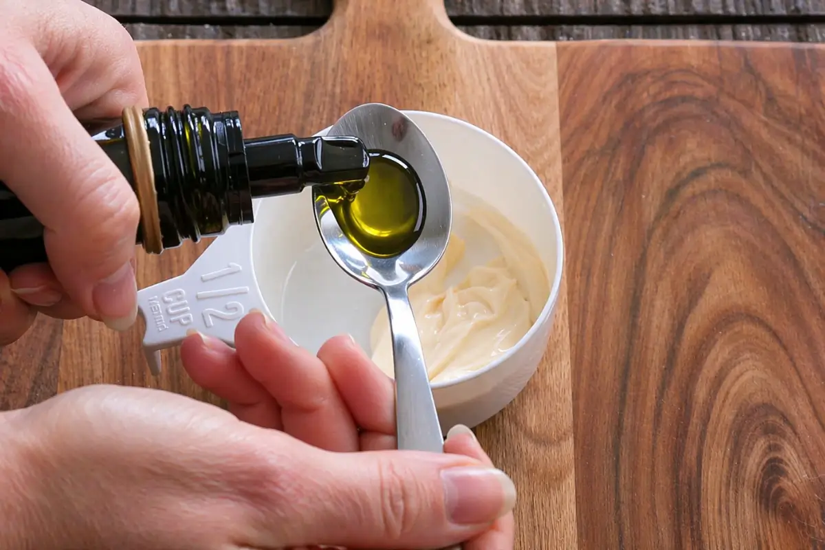 Garlic-infused olive oil being added to mayonnaise to prepare a smooth aioli.