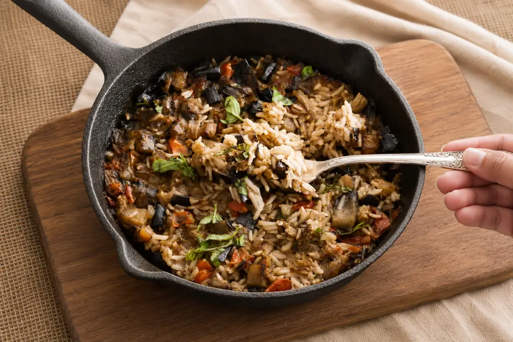Fork lifting One-Pot Mediterranean Eggplant Rice from a cast-iron skillet.