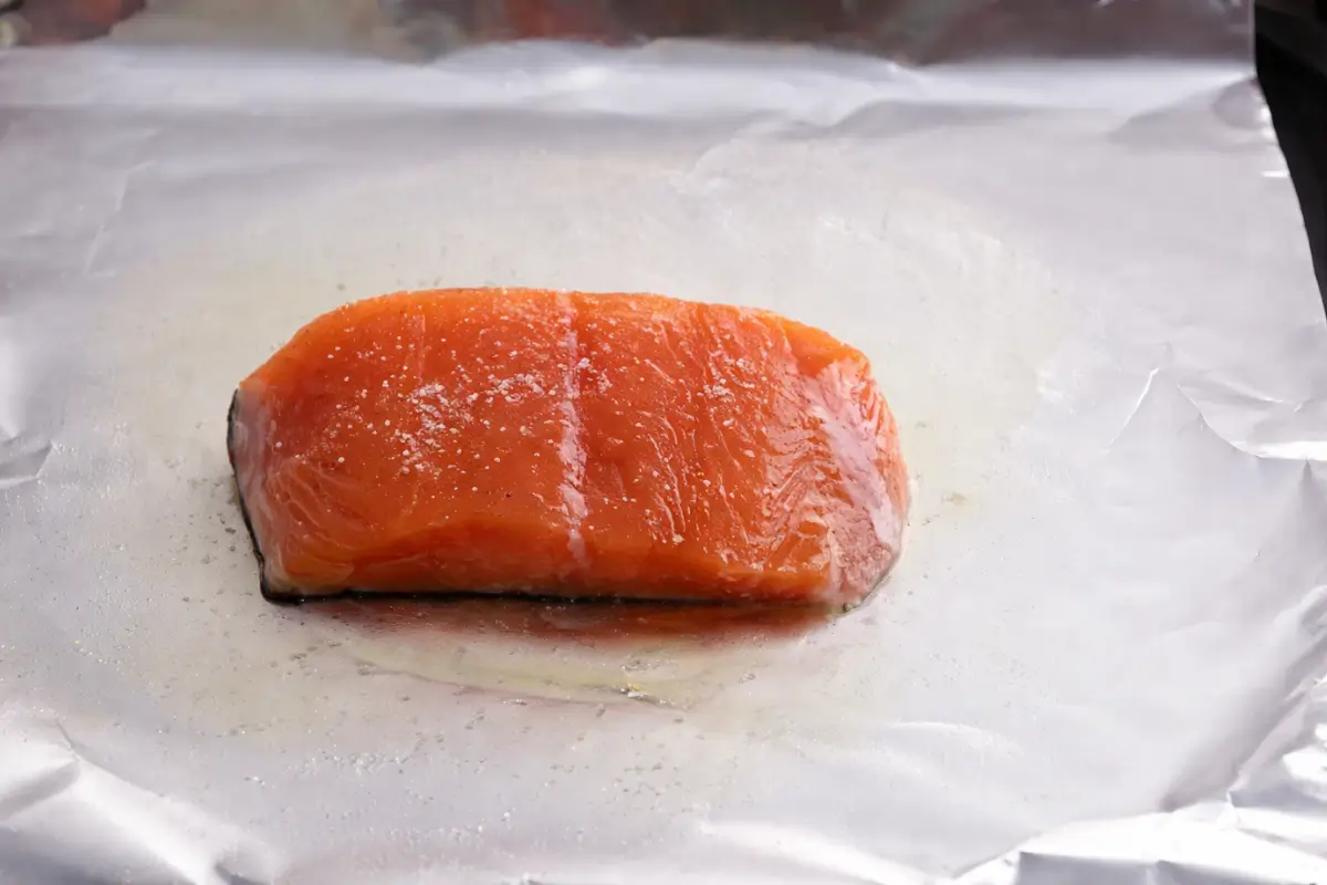 Fresh salmon fillet lightly seasoned with salt and placed on foil before baking.