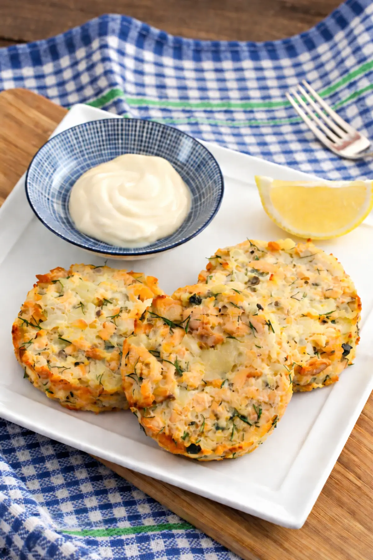 Three golden salmon patties served with a creamy dipping sauce and a wedge of lemon on a white plate.