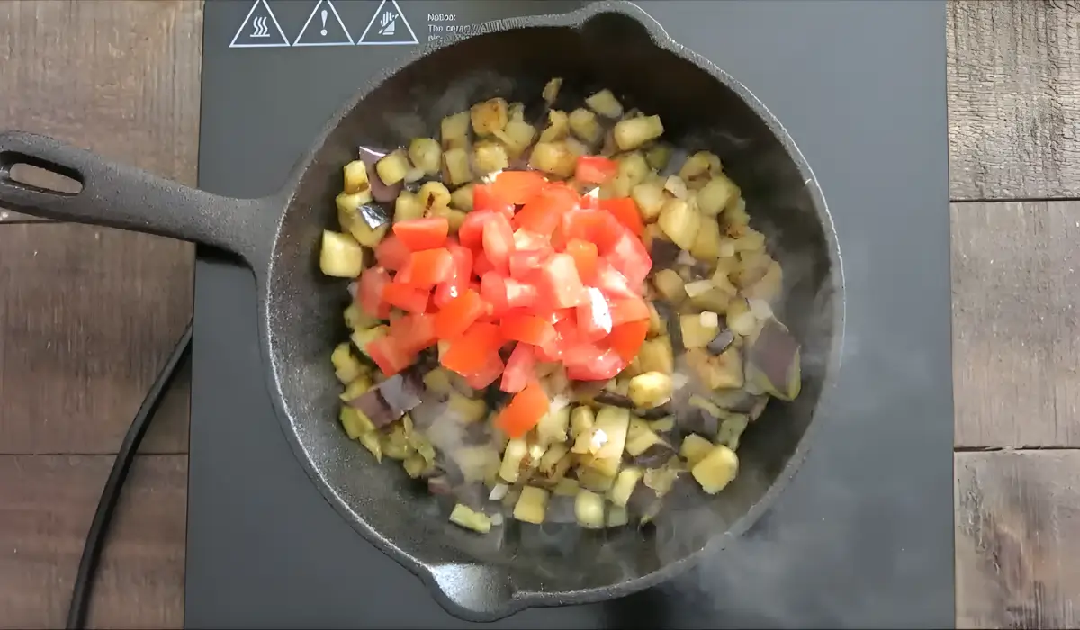 Sautéed eggplant in a skillet with fresh tomatoes added on top.
