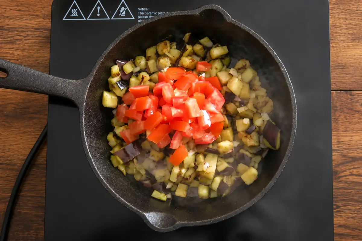 Chopped tomatoes added to softened eggplant and onions in a cast-iron skillet.