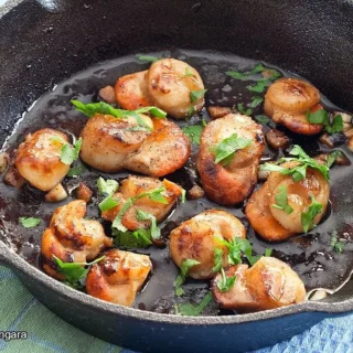 Golden scallops topped with fresh parsley and garlic butter inside a skillet.