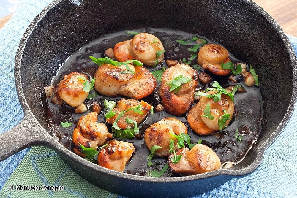 Golden scallops topped with fresh parsley and garlic butter inside a skillet.