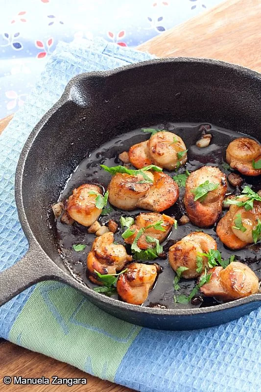 Pan-seared scallops with garlic and parsley in a cast-iron skillet.