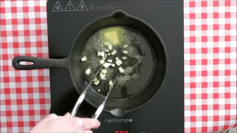 Garlic pieces sizzling in melted butter in a black skillet.