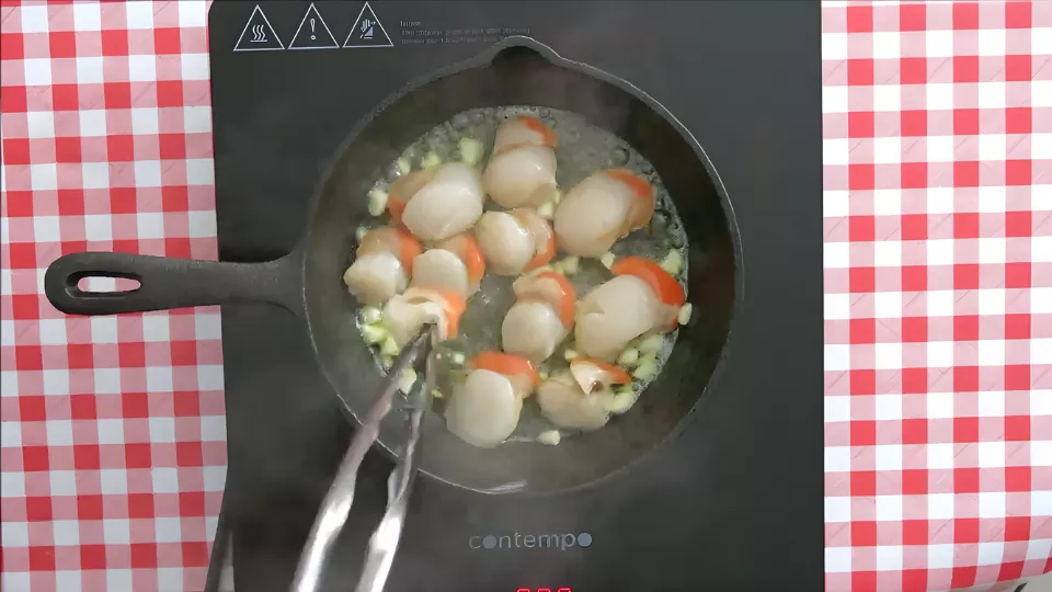 Scallops with roe searing in garlic butter in a black skillet over medium-high heat.