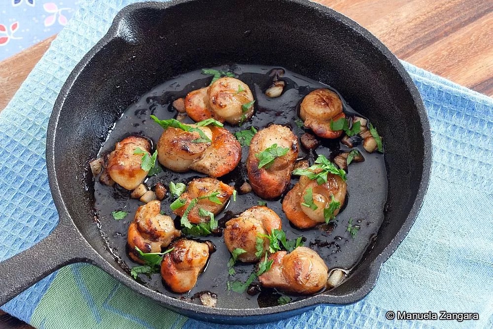 Cooked scallops in garlic butter garnished with chopped parsley, served in a skillet.
