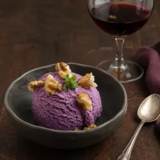 Scoop of Malbec ice cream topped with walnuts and a sprig of fresh mint, served with a glass of red wine.