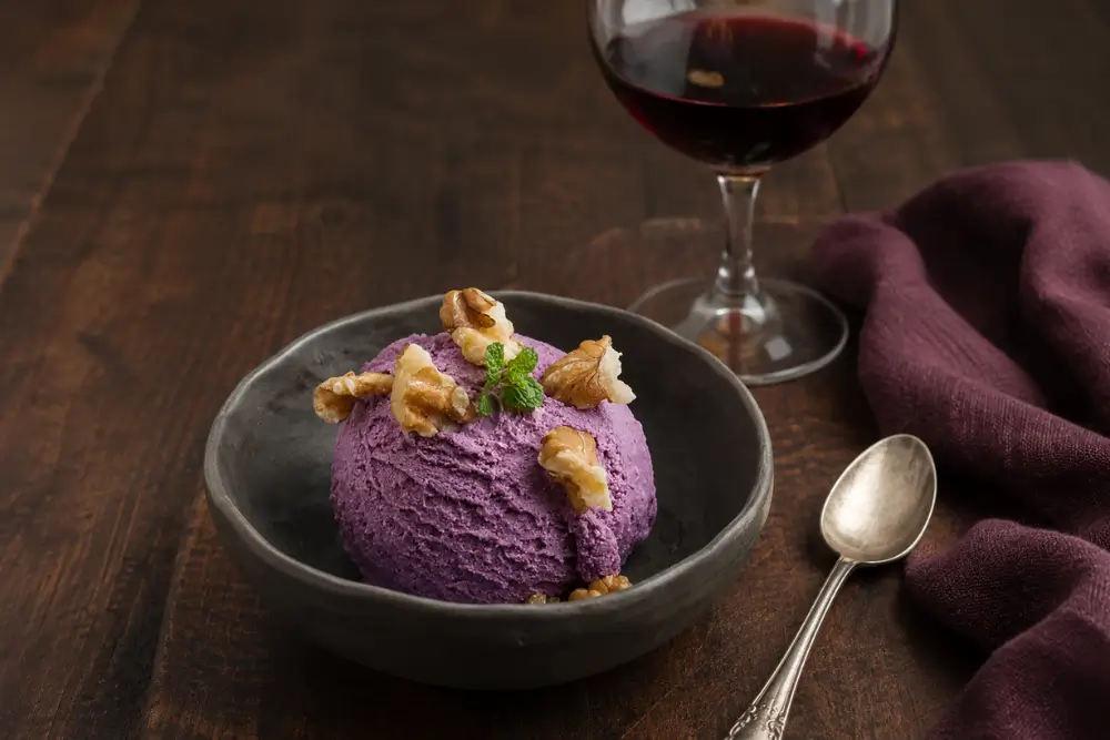 Scoop of Malbec ice cream topped with walnuts and a sprig of fresh mint, served with a glass of red wine.