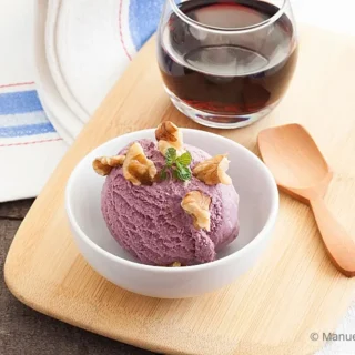 Bowl of purple Malbec ice cream beside a glass of wine on a wooden board.