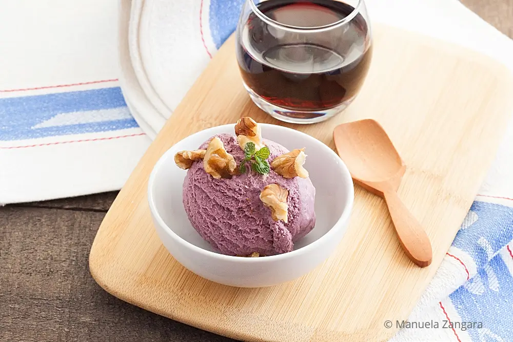Bowl of purple Malbec ice cream beside a glass of wine on a wooden board.