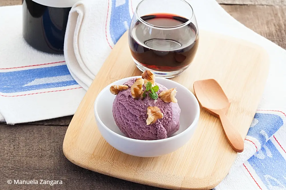 Red wine with ice cream topped with walnuts, served on a wooden board.