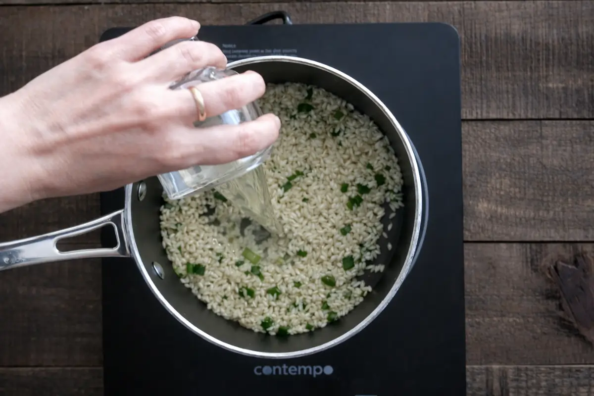 Pouring liquid into rice while cooking risotto calamari in a saucepan.