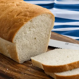 Sliced White Sandwich Bread on a wooden board beside a serrated bread knife.