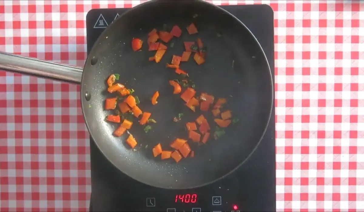Chopped capsicum softening in a non-stick frying pan.
