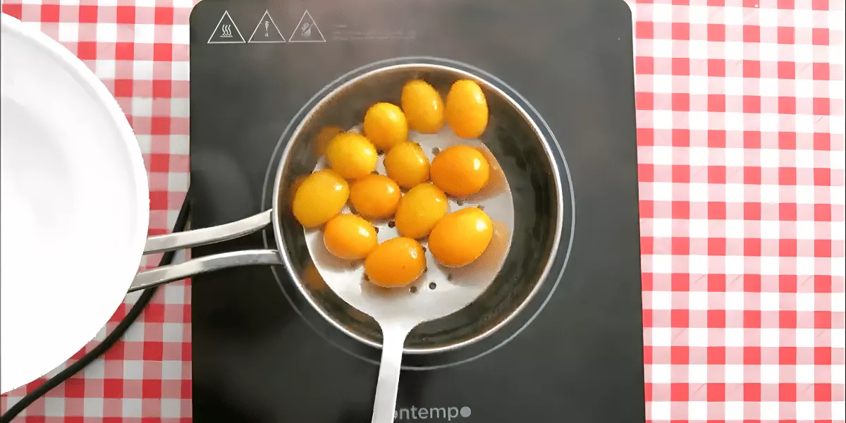 Cooked kumquats being lifted from hot water with a slotted spoon after boiling.