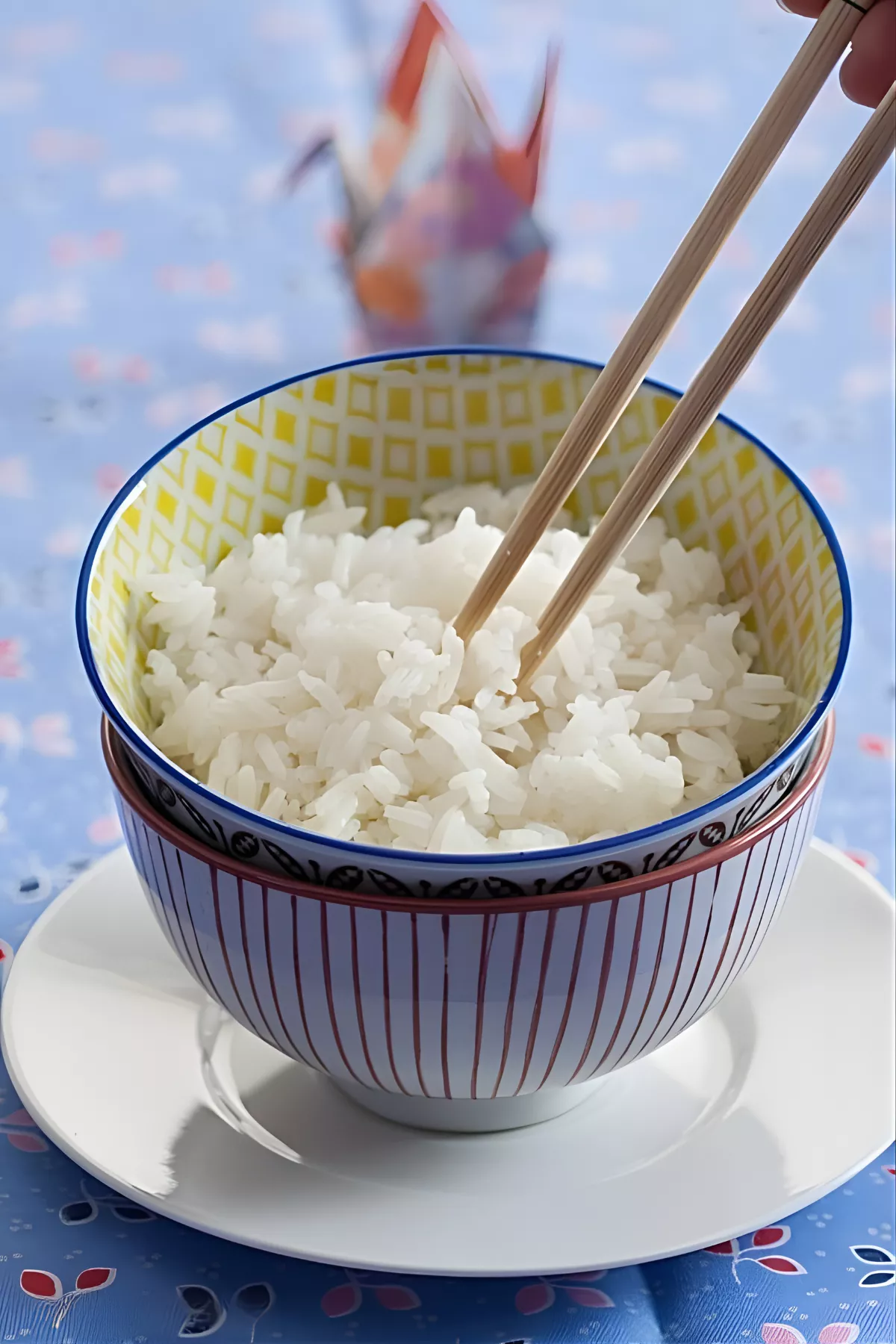 Chopsticks lifting fluffy long grain rice from a patterned bowl.