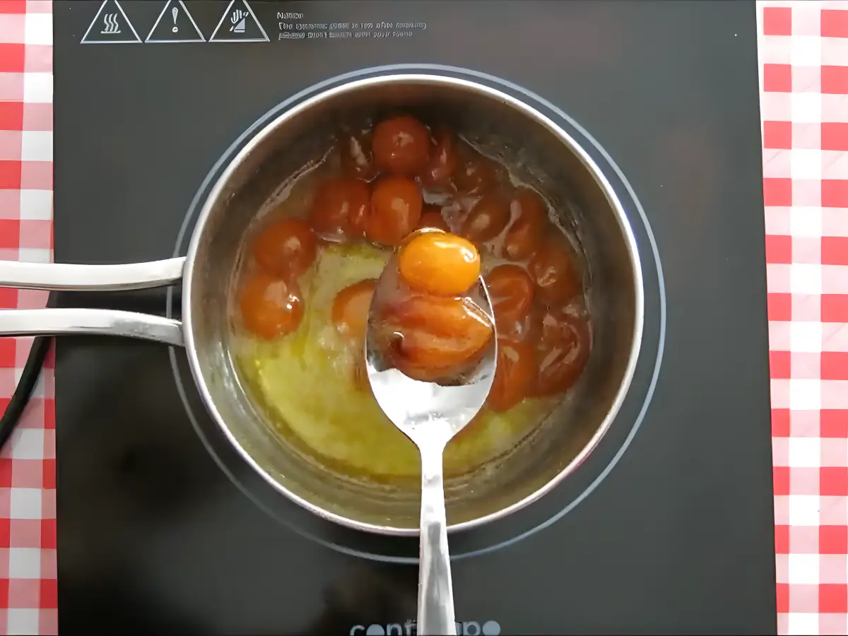 Cooked kumquats in thick syrup being lifted with a spoon to show their glossy, translucent texture.