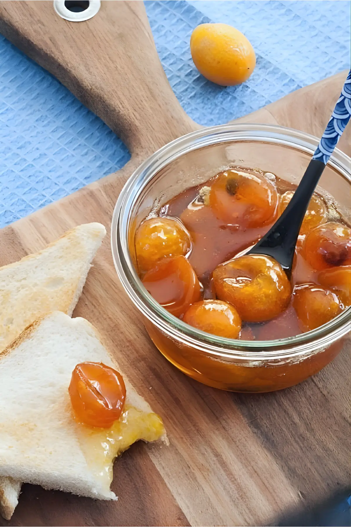 Overhead view of kumquat jam in a jar served with slices of toast on a wooden board.