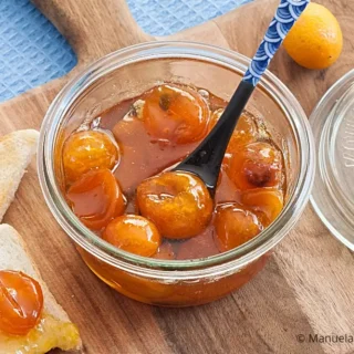 Kumquat jam in a jar with toast and fresh kumquats arranged on a wooden board.