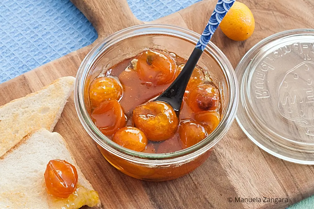 Kumquat jam in a jar with toast and fresh kumquats arranged on a wooden board.