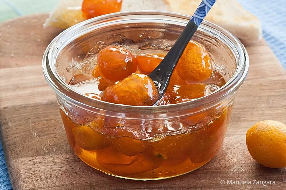 A jar of kumquat jam with a spoon and toast in the background.