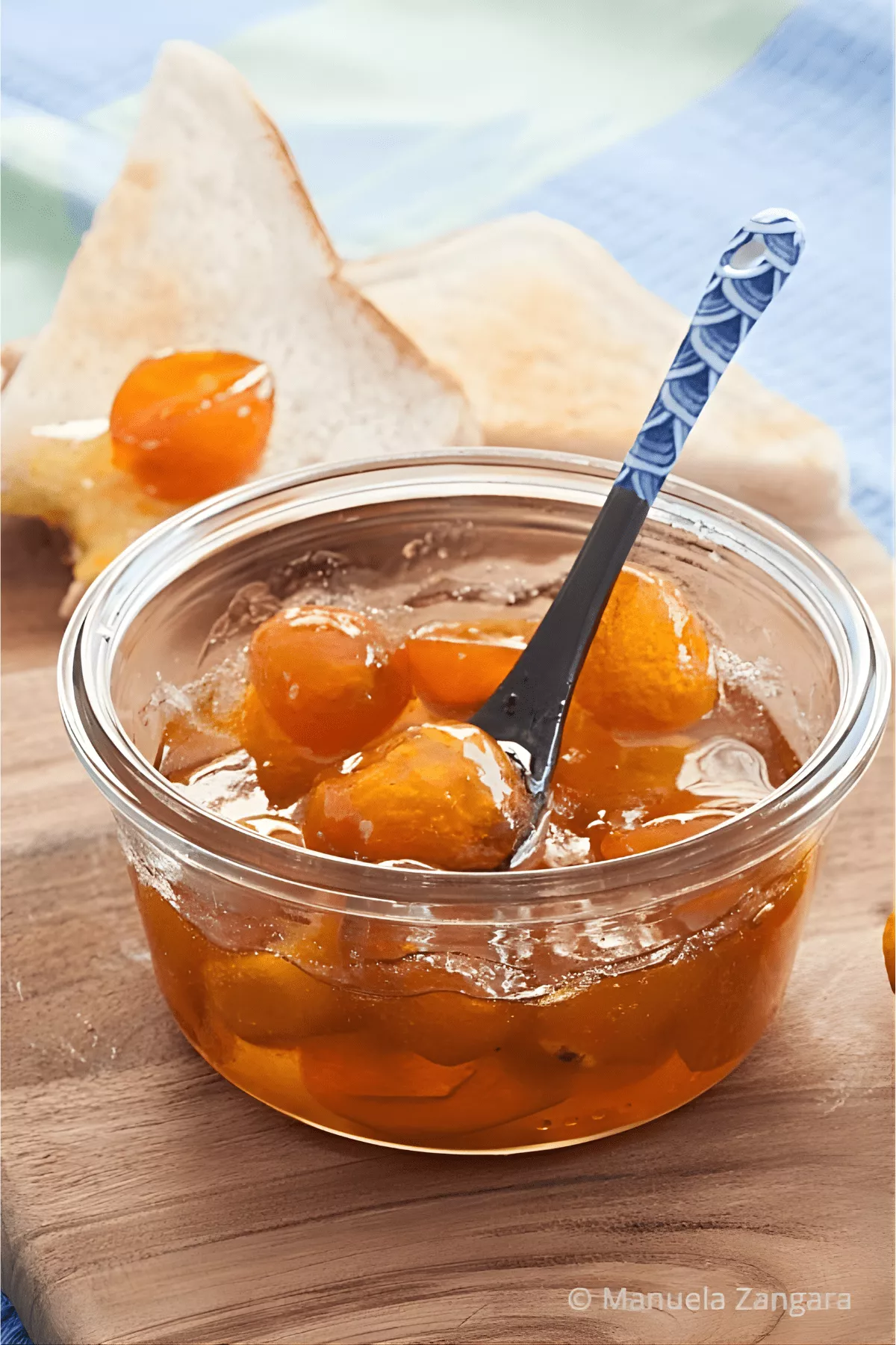 Vertical photo of kumquat jam in a glass jar with toast and a blue spoon.