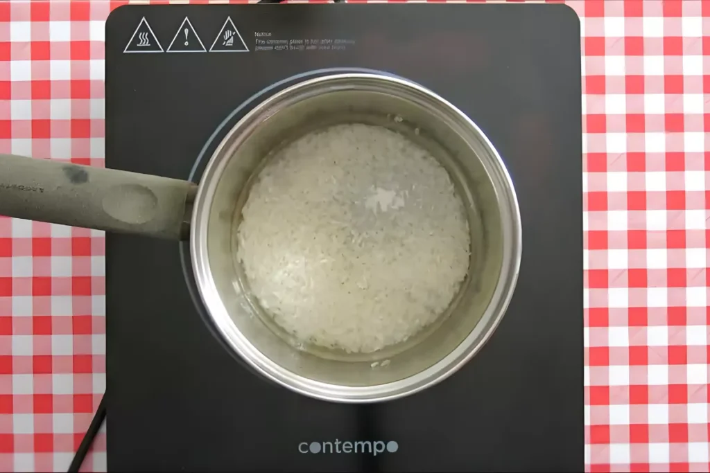 Long grain rice simmering gently in a pot of water on the stove.