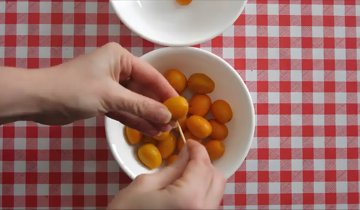 Hands pricking small holes in fresh kumquats with a toothpick before boiling.