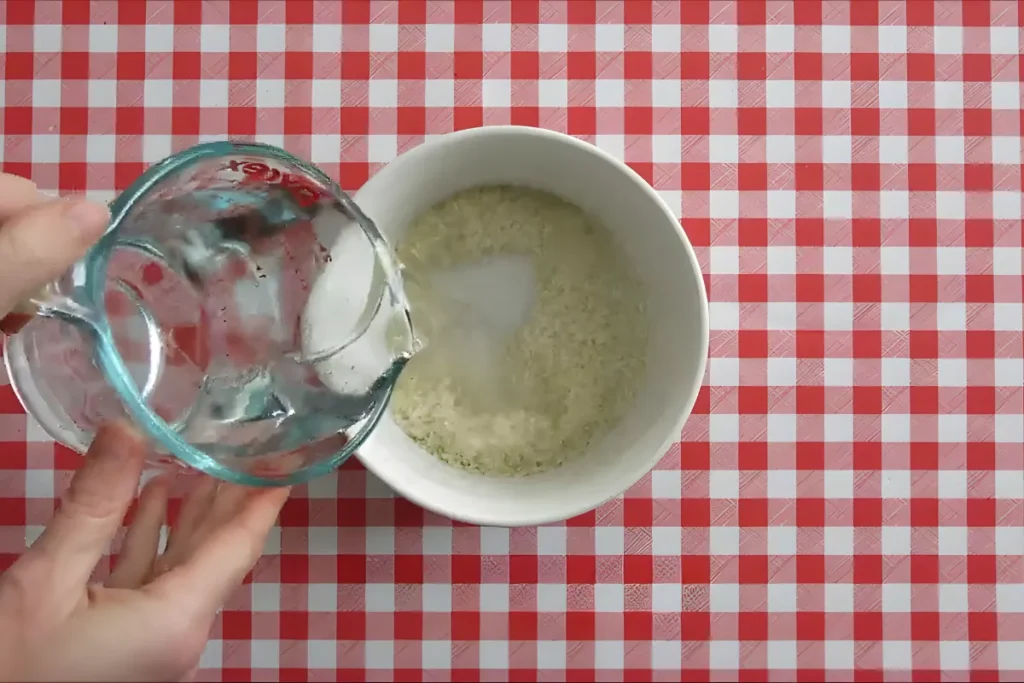 Pouring water into a bowl of long grain rice to rinse away excess starch.