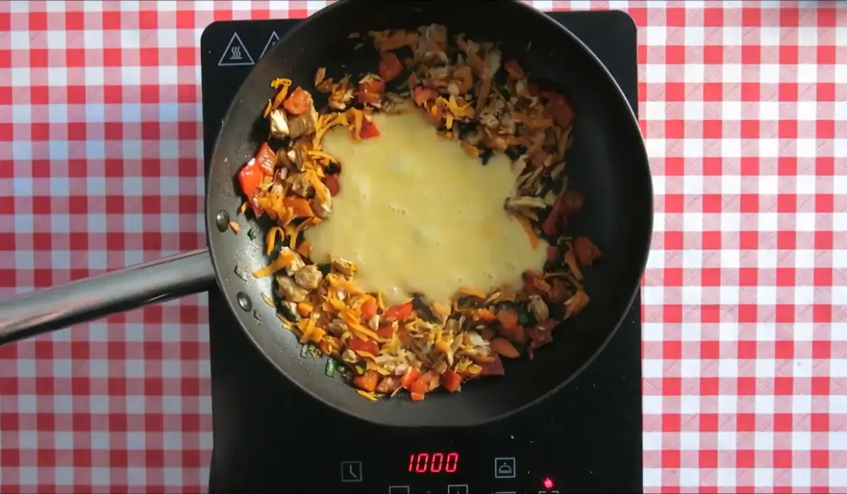 Egg being scrambled in the centre of a pan with vegetables pushed aside.